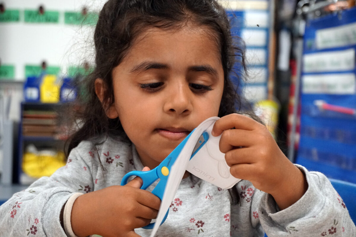 A Castro Valley Unified School District TK student uses scissors to cut a square by following the lines on the paper.